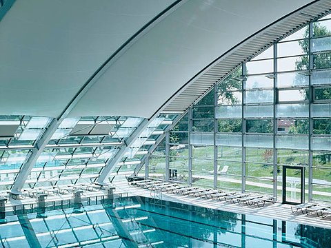 Schwimmhalle mit heller Membrandecke über dem Becken und raumhoher Glasfassade