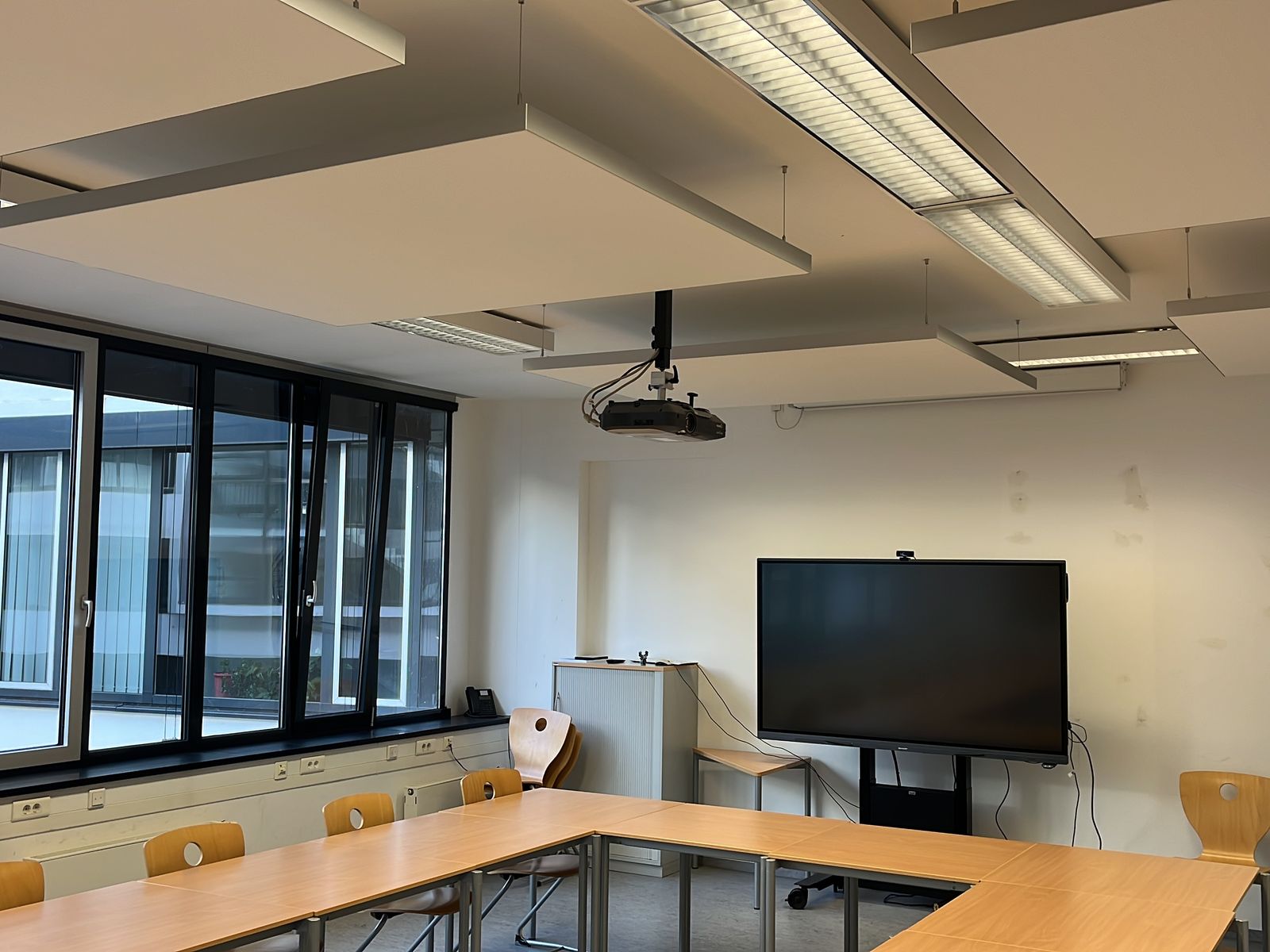 Seminarraum mit abgehängten Deckensegeln über U-förmiger Tischordnung und Präsentationsdisplay
