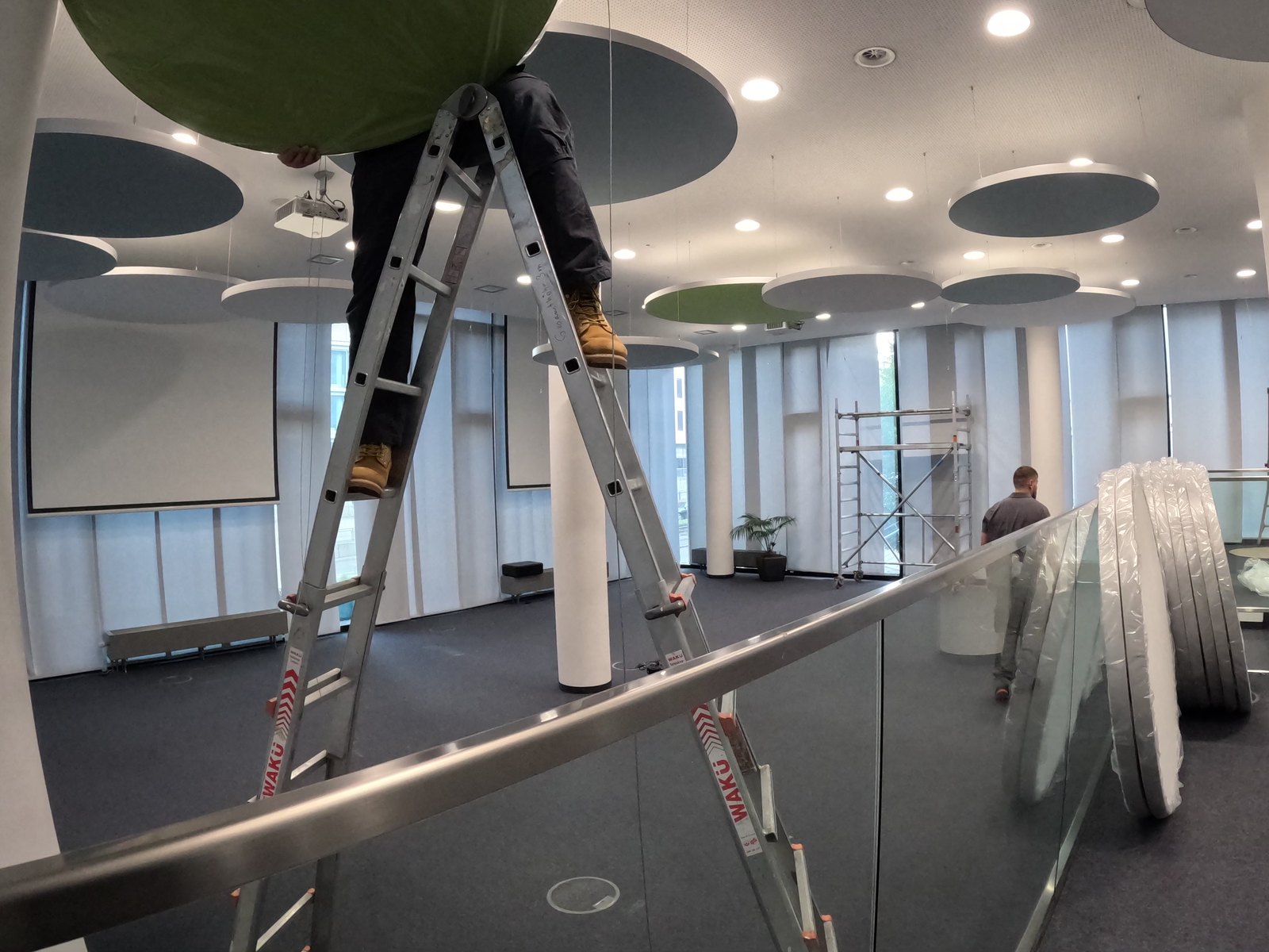 Ein grünes rundes Deckensegel wird über eine Leiter zur Decke angehoben