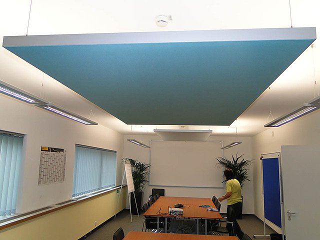 Großes blaues Akustik-Deckensegel über einem Schulungsraum mit Tischinseln