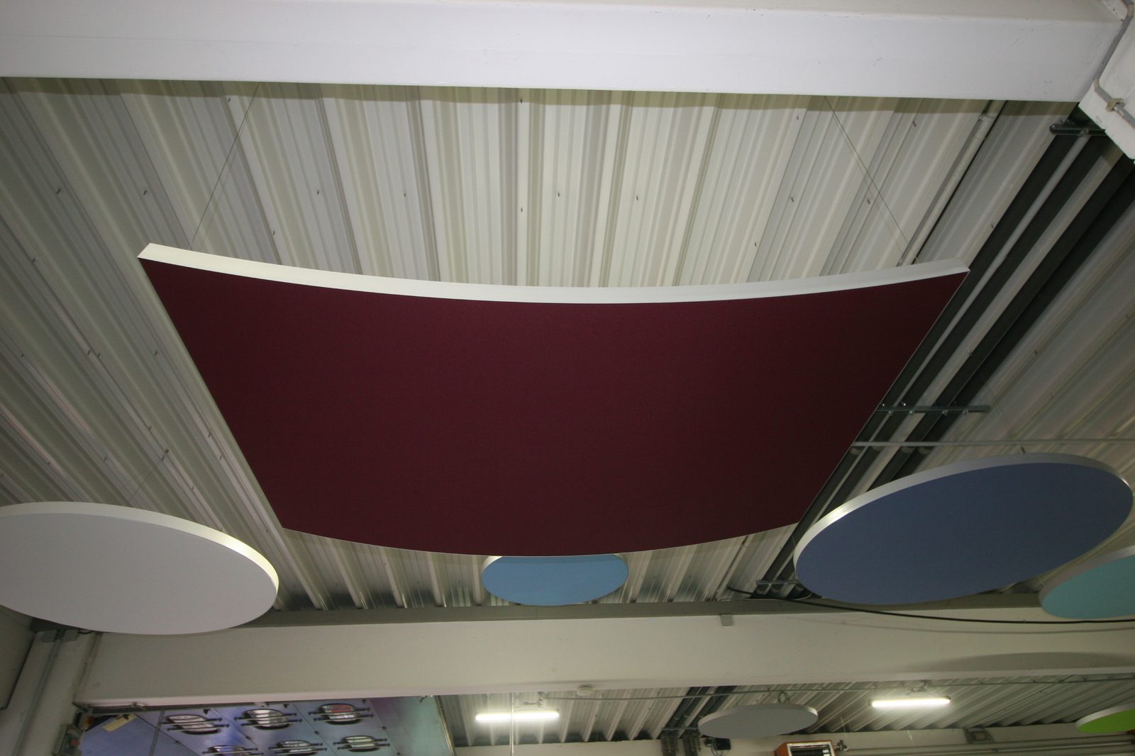 Gebogenes Deckensegel in Bordeaux unter einer Trapezblechdecke, darunter runde Segel in Hellblau