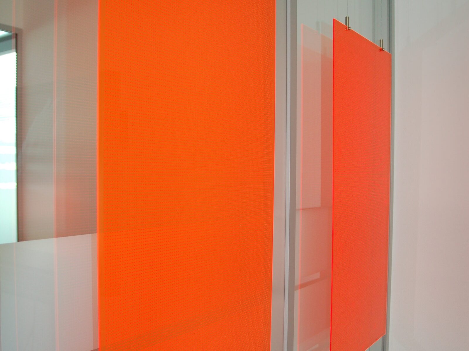 Orange eingefärbte, mikrogelochte PLEXIGLAS®-Elemente vor einer Glaswand